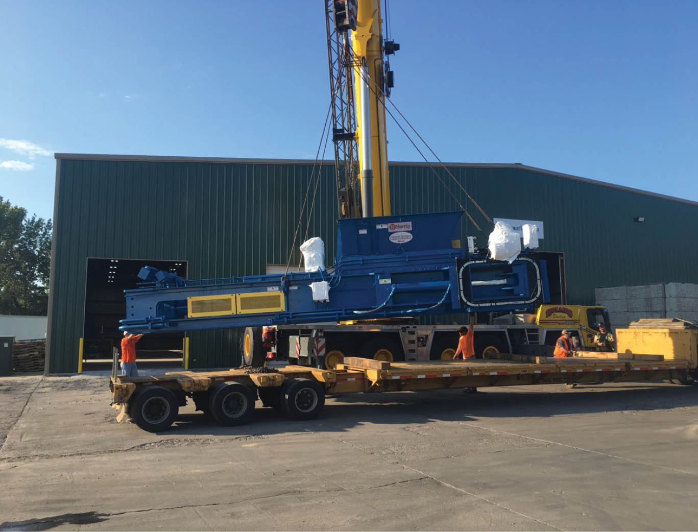 Harris two-ram baler being moved off a truck by crane during install