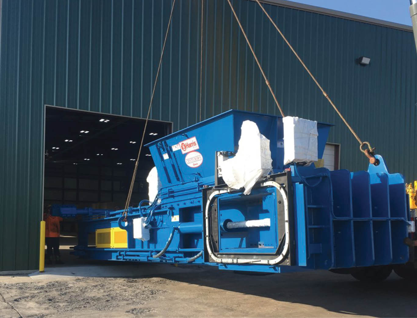 Harris two-ram baler being moved by crane into a building for installation