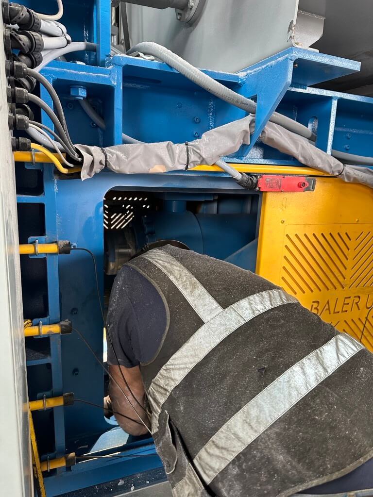 HSC technician performing preventative maintenance on a single-ram open-end auto-tie baler