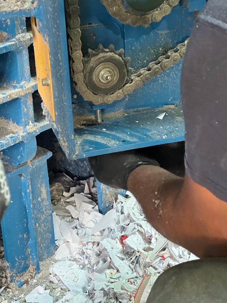 HSC technician performing preventative maintenance on a single-ram open-end auto-tie baler at a paper recycling facility